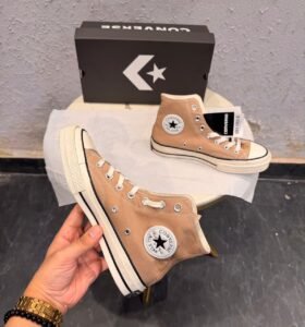 Beige high-top canvas-style sneakers with cream laces, metal eyelets, an off-white midsole with black pinstripes, and a dark brown patterned outsole