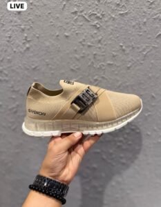 Beige slip-on sneakers with a metallic silver-tone buckle, broad front strap, and sculpted white outsole