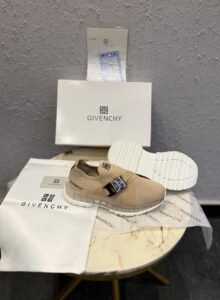 Beige slip-on sneakers with a metallic silver-tone buckle, broad front strap, and sculpted white outsole