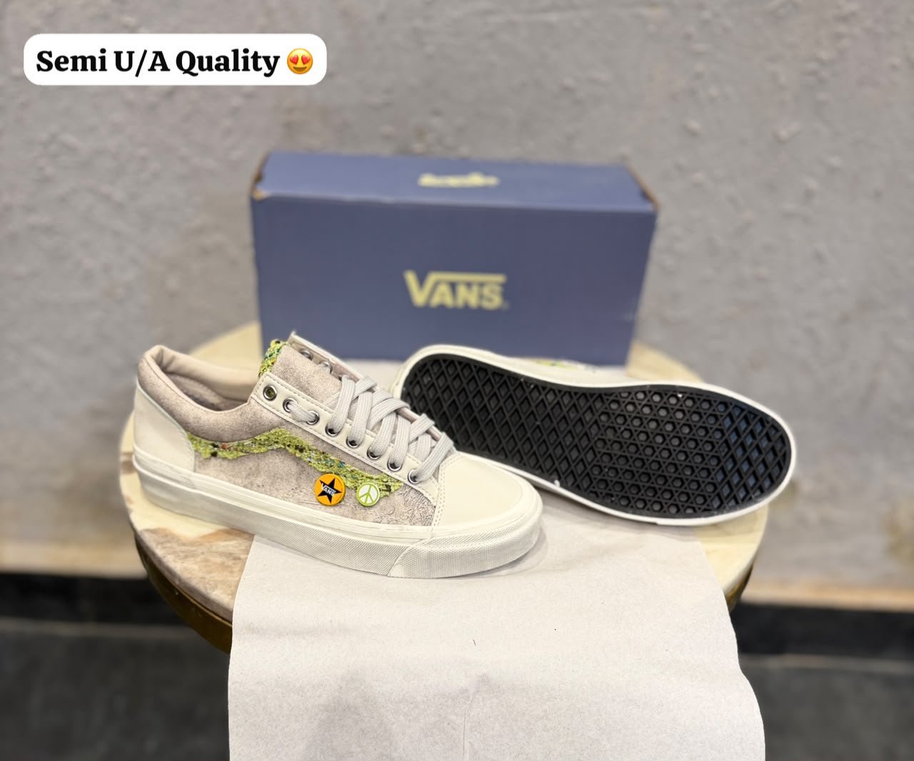 Beige low-top sneakers with green textured side detailing, decorative circular badges, cream toe panels, and a black patterned outsole