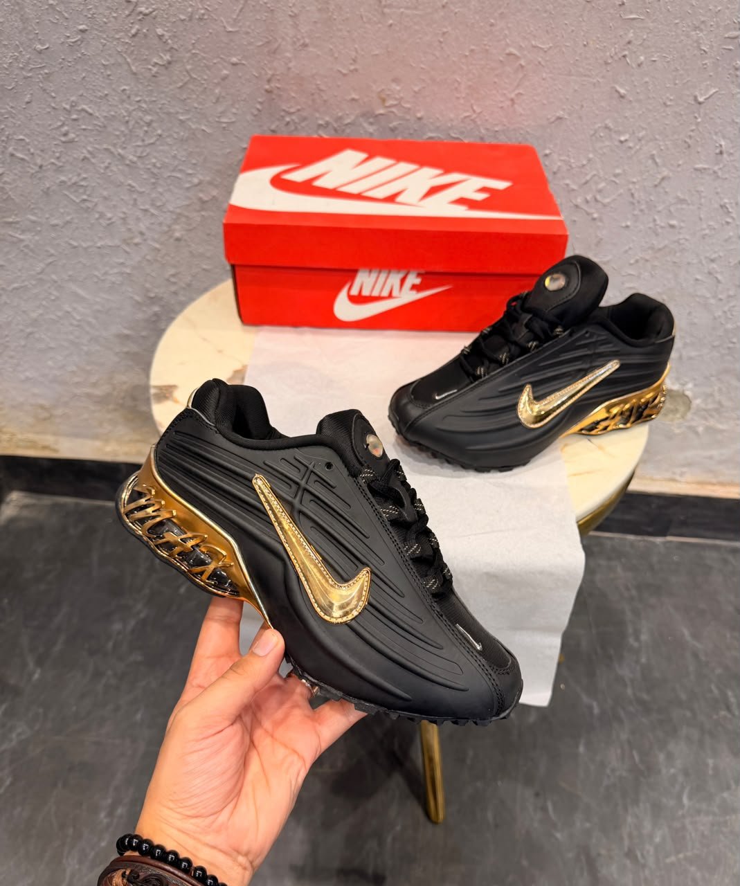Black sneakers with sculpted side panels, metallic gold accents, and a decorative gold heel section