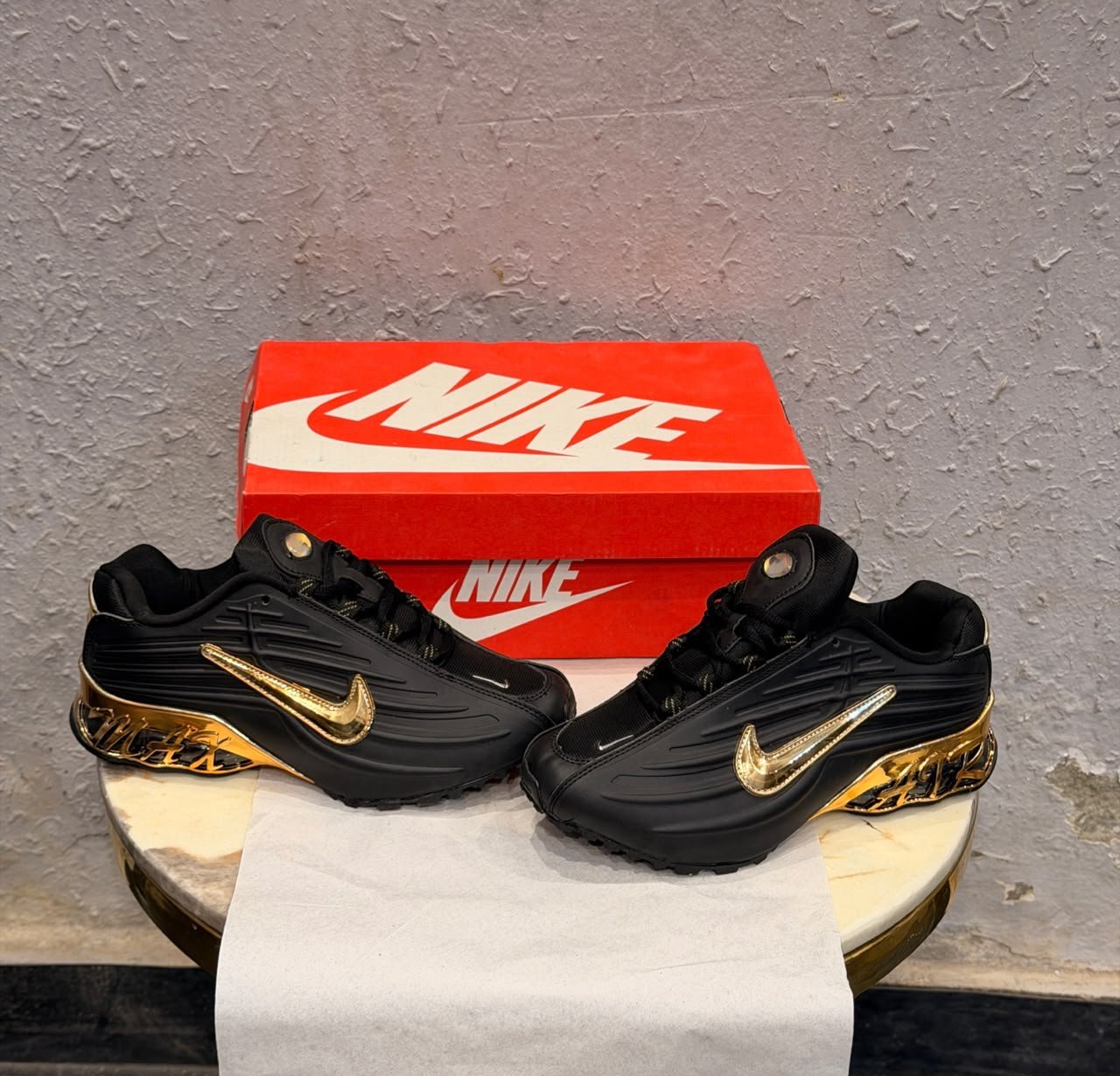 Black sneakers with sculpted side panels, metallic gold accents, and a decorative gold heel section