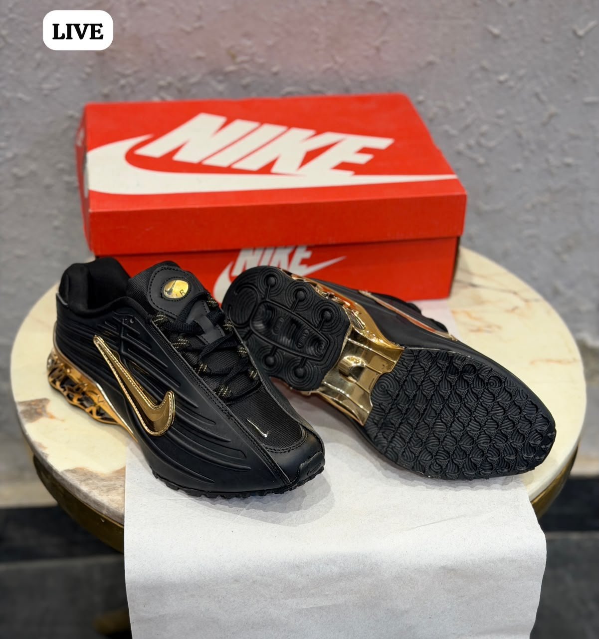 Black sneakers with sculpted side panels, metallic gold accents, and a decorative gold heel section