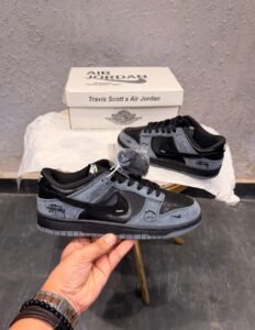 Black and charcoal grey low-top sneakers with layered panels, a perforated toe, grey outsole, and additional black laces.