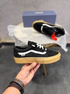 Black low-top sneakers with white side detailing, white laces, checkerboard-inspired heel accents, and a gum-coloured sole