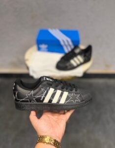 Black low-top sneakers with cream-coloured stripes, decorative star stitching, and a textured shell-shaped toe cap