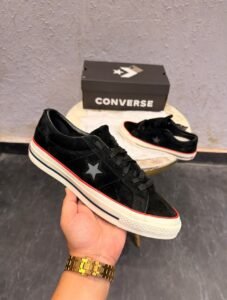 Black low-top sneakers with a textured suede-look upper, star-shaped side detail, cream sole, and red accent stripe