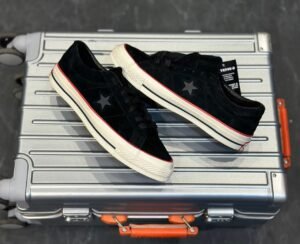 Black low-top sneakers with a textured suede-look upper, star-shaped side detail, cream sole, and red accent stripe