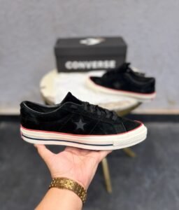 Black low-top sneakers with a textured suede-look upper, star-shaped side detail, cream sole, and red accent stripe