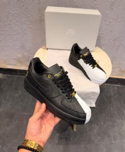 Black and white low-top sneakers with contrasting panels, gold-tone eyelets, decorative lace accessories, and patterned outsoles