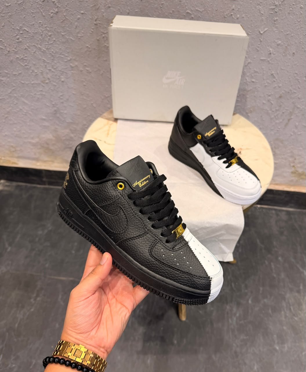 Black and white low-top sneakers with contrasting panels, gold-tone eyelets, decorative lace accessories, and patterned outsoles