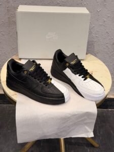 Black and white low-top sneakers with contrasting panels, gold-tone eyelets, decorative lace accessories, and patterned outsoles