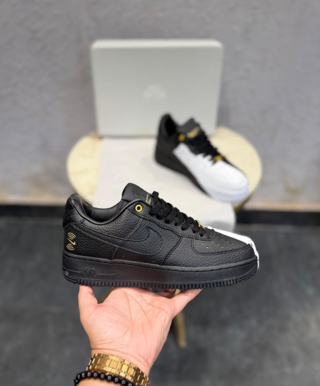 Black and white low-top sneakers with contrasting panels, gold-tone eyelets, decorative lace accessories, and patterned outsoles