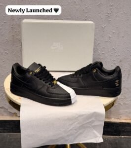 Black and white low-top sneakers with contrasting panels, gold-tone eyelets, decorative lace accessories, and patterned outsoles