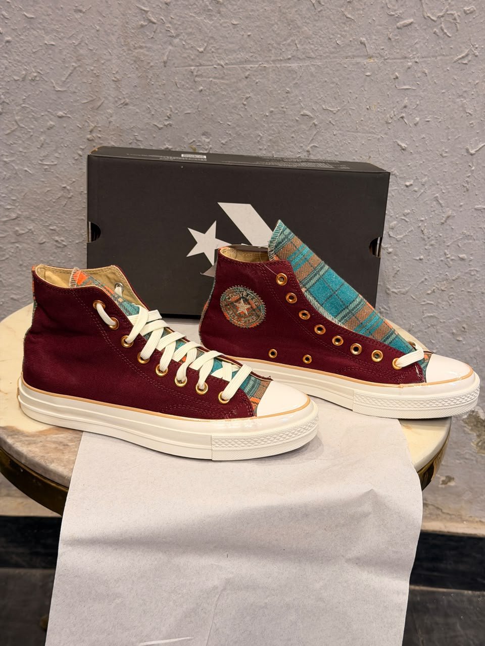 Burgundy high-top canvas sneakers with teal multicolour plaid accents, gold-tone eyelets, decorative side patches, and white rubber soles