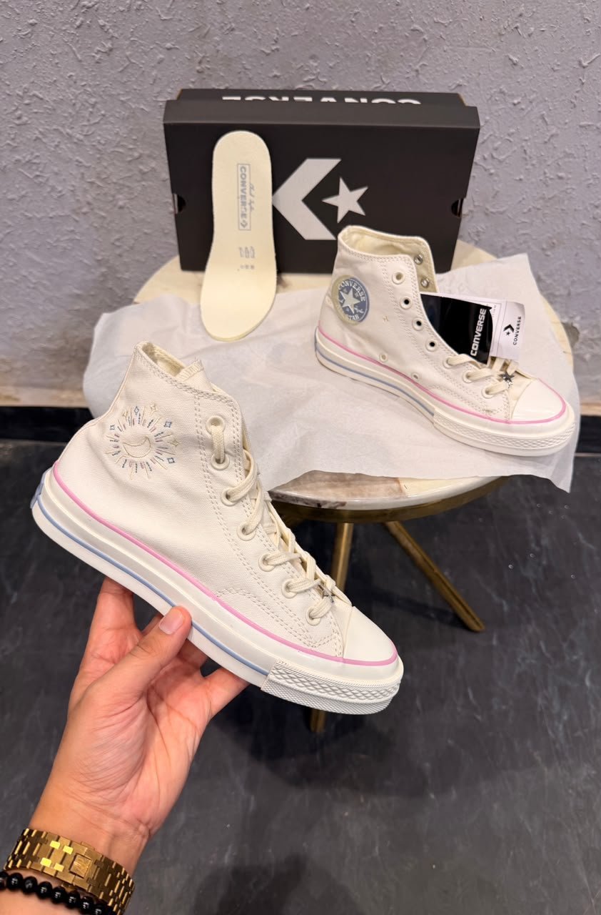 Celestial white high-top sneakers with pink trim, blue ankle emblem, and yellow outsole