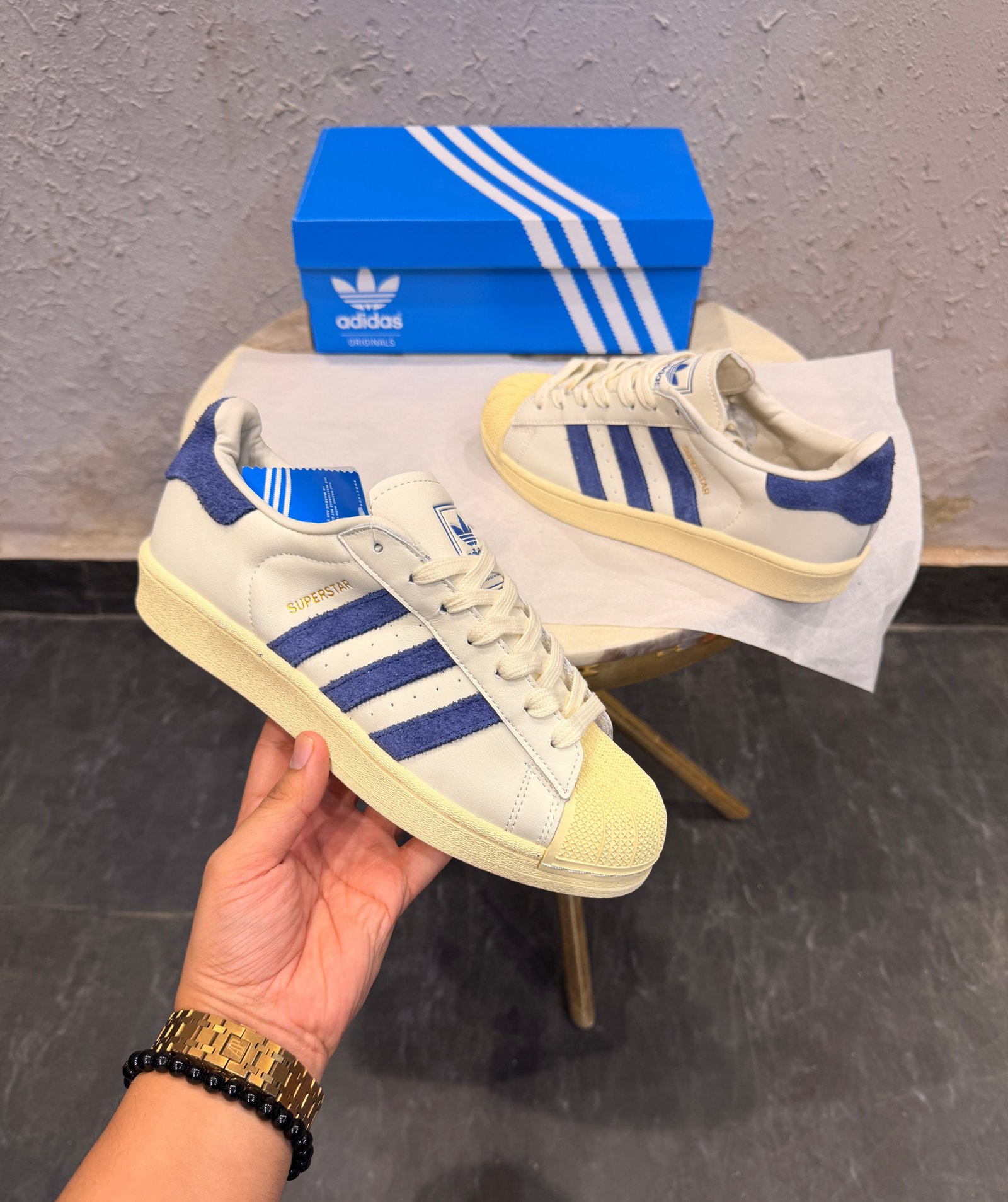 Cream and royal blue low-top sneakers with contrasting blue stripes, cream laces, and a textured shell-shaped toe cap