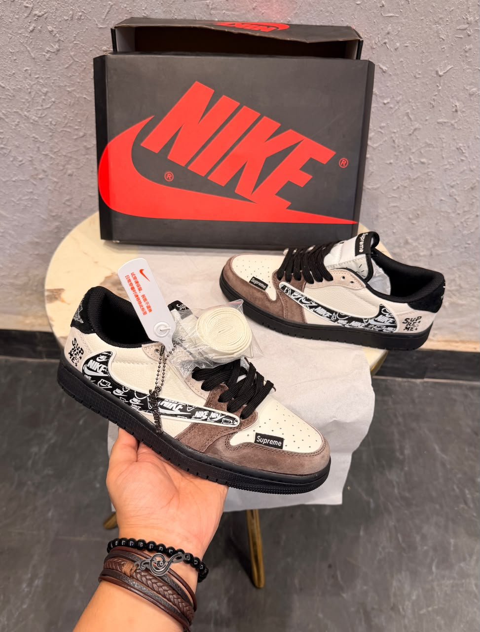 Cream and brown low top sneakers with layered overlays, black laces, patterned side detailing, and a black textured outsole