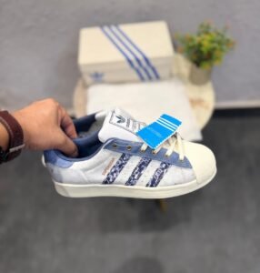 White and blue denim-style low-top sneakers featuring patterned side stripes, cream laces, and a textured shell-style toe.