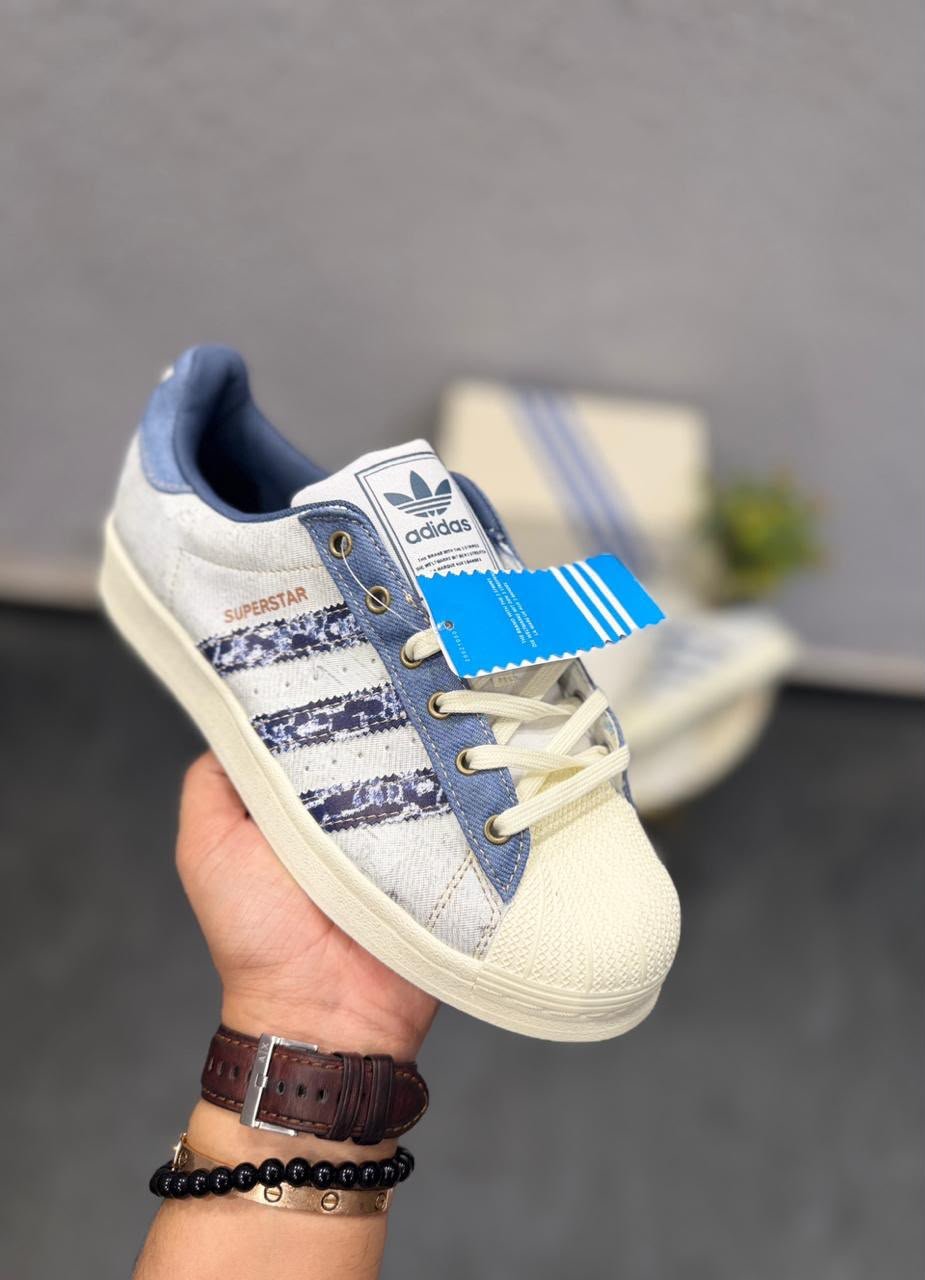 White and blue denim-style low-top sneakers featuring patterned side stripes, cream laces, and a textured shell-style toe.