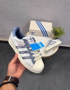 White and blue denim-style low-top sneakers featuring patterned side stripes, cream laces, and a textured shell-style toe.
