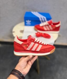 Red low-top retro sneakers with cream-coloured stripes, cream laces, gum-brown outsoles, and an additional pair of red laces