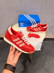 Red low-top retro sneakers with cream-coloured stripes, cream laces, gum-brown outsoles, and an additional pair of red laces