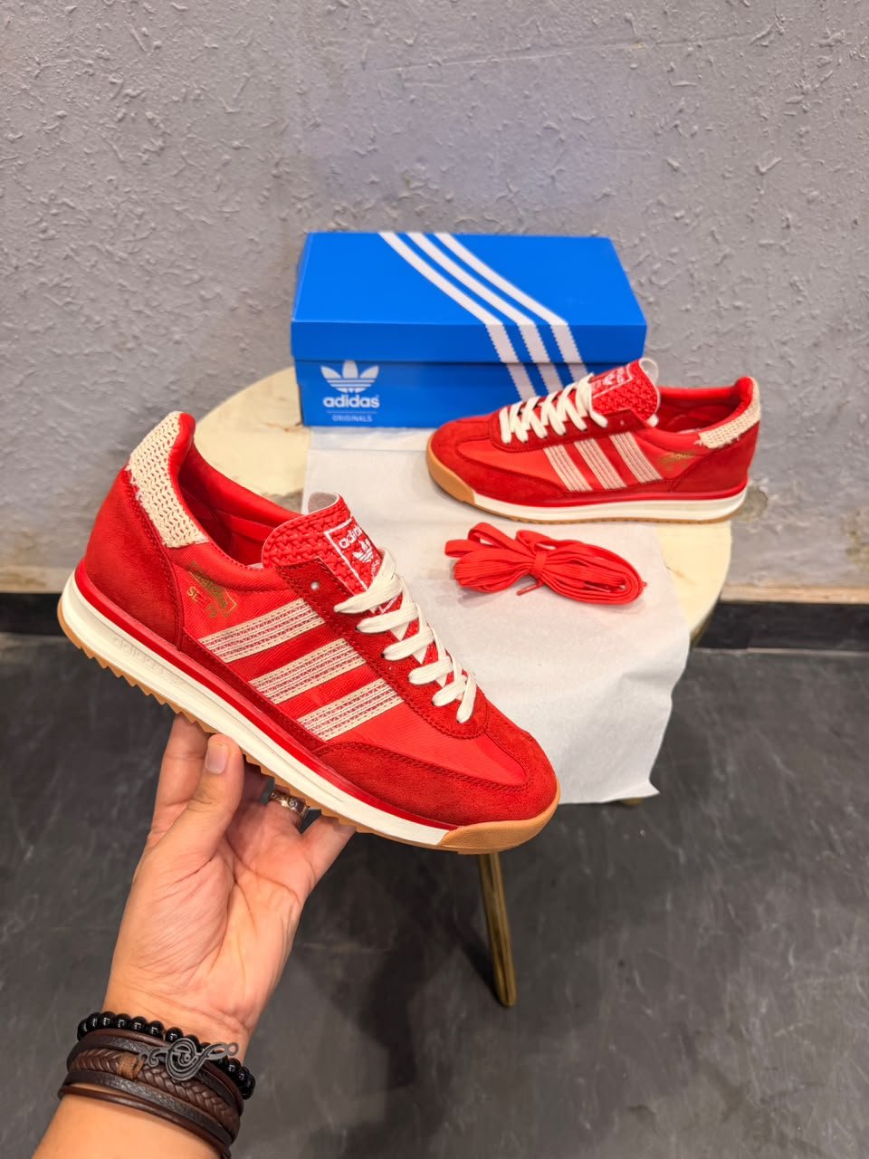 Red low-top retro sneakers with cream-coloured stripes, cream laces, gum-brown outsoles, and an additional pair of red laces