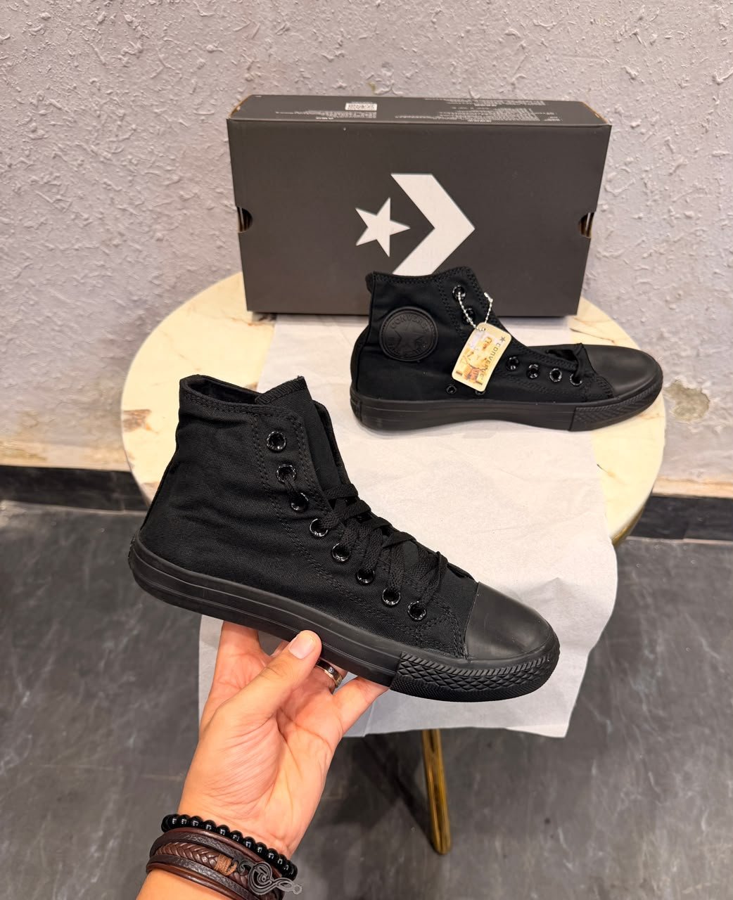 Triple black high top sneakers with a black canvas-style upper, matching laces, dark metal eyelets, textured toe cap, and patterned black outsole