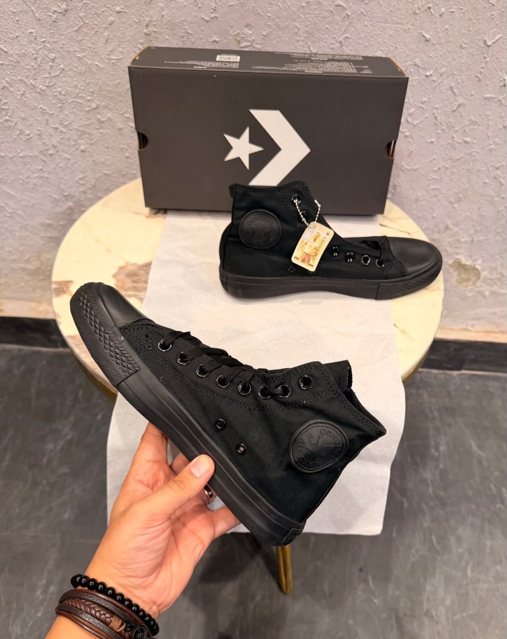 Triple black high top sneakers with a black canvas-style upper, matching laces, dark metal eyelets, textured toe cap, and patterned black outsole