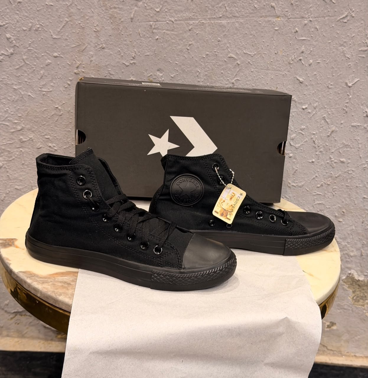 Triple black high top sneakers with a black canvas-style upper, matching laces, dark metal eyelets, textured toe cap, and patterned black outsole
