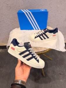 White and navy low-top sneakers with patterned side panels, white laces, and a textured shell-shaped toe cap