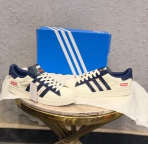 White and navy low-top sneakers with patterned side panels, white laces, and a textured shell-shaped toe cap