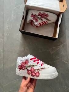 White low-top sneakers with raised floral embroidery in red-pink and deep blue colourways
