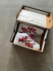 White low-top sneakers with raised floral embroidery in red-pink and deep blue colourways