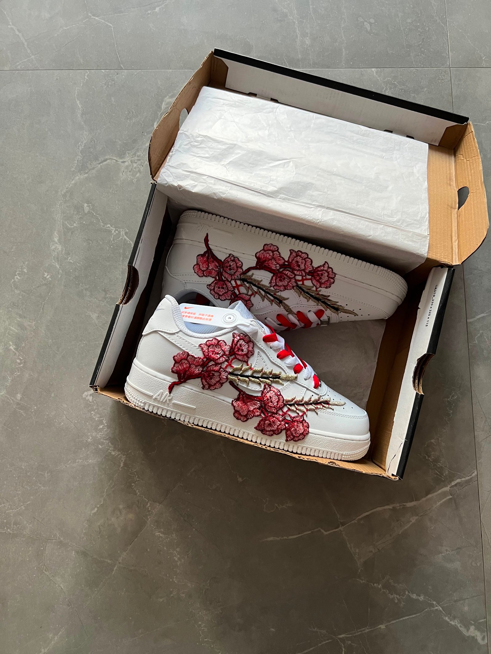 White low-top sneakers with raised floral embroidery in red-pink and deep blue colourways