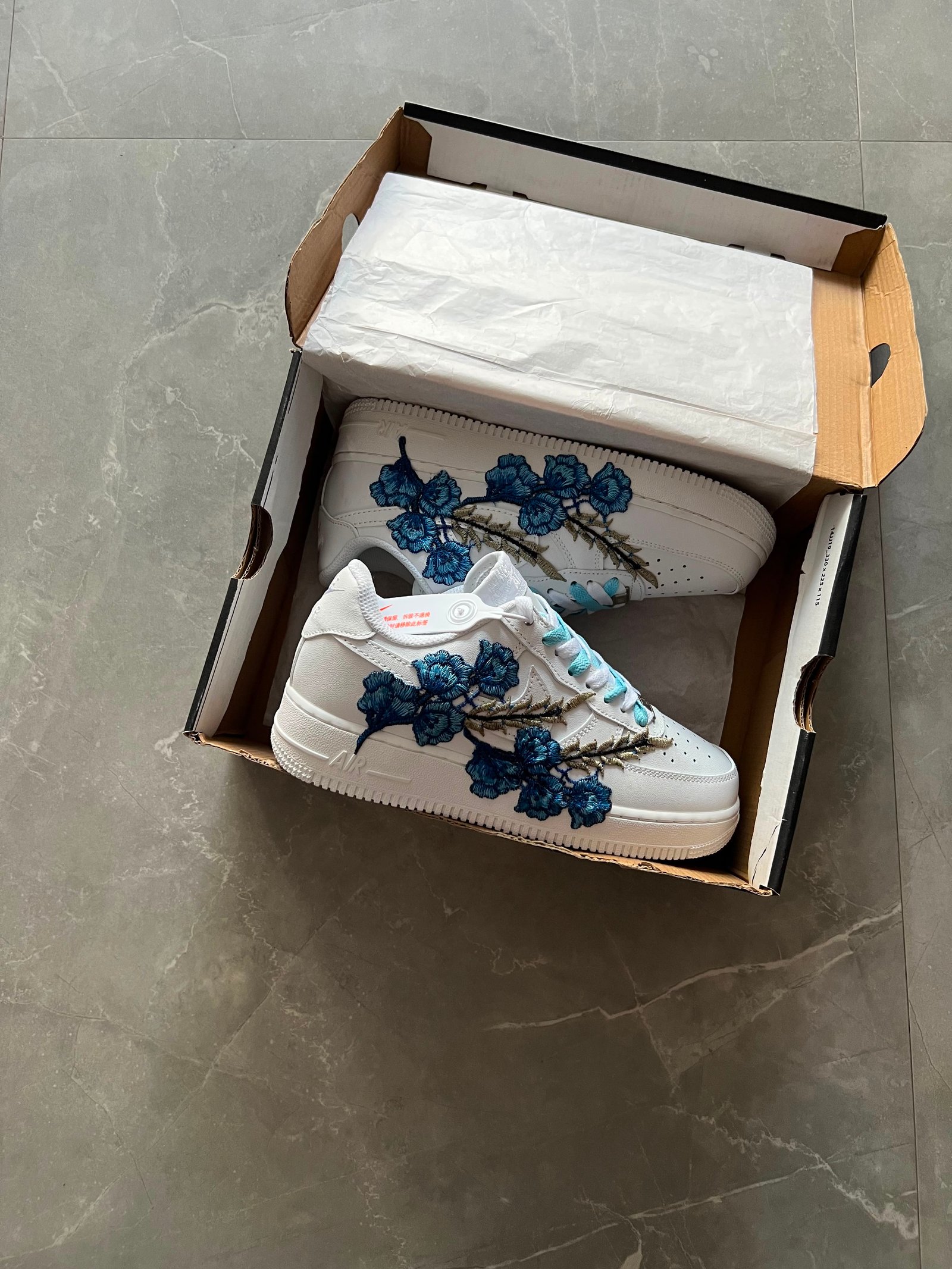 White low-top sneakers with raised floral embroidery in red-pink and deep blue colourways