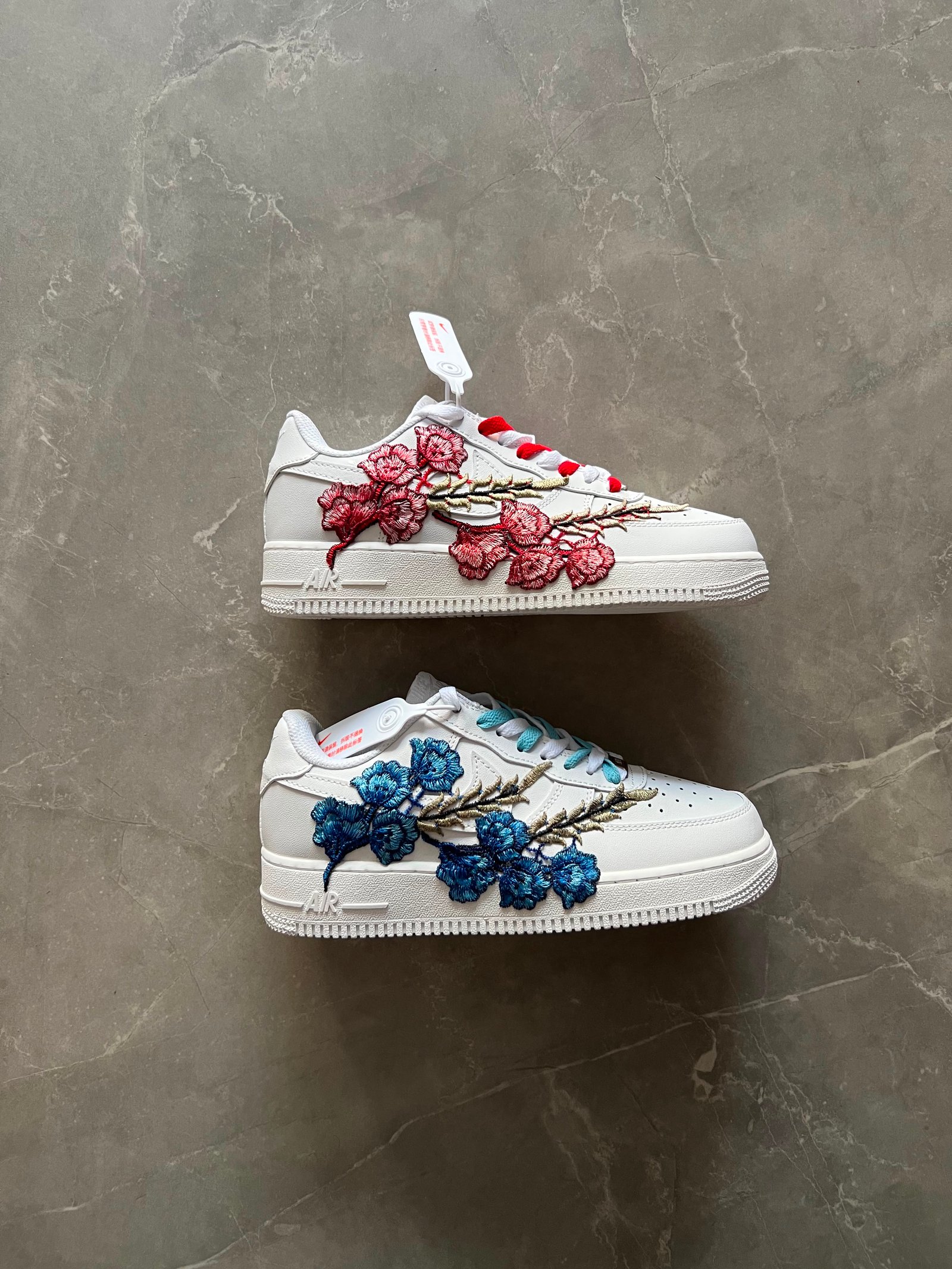 White low-top sneakers with raised floral embroidery in red-pink and deep blue colourways