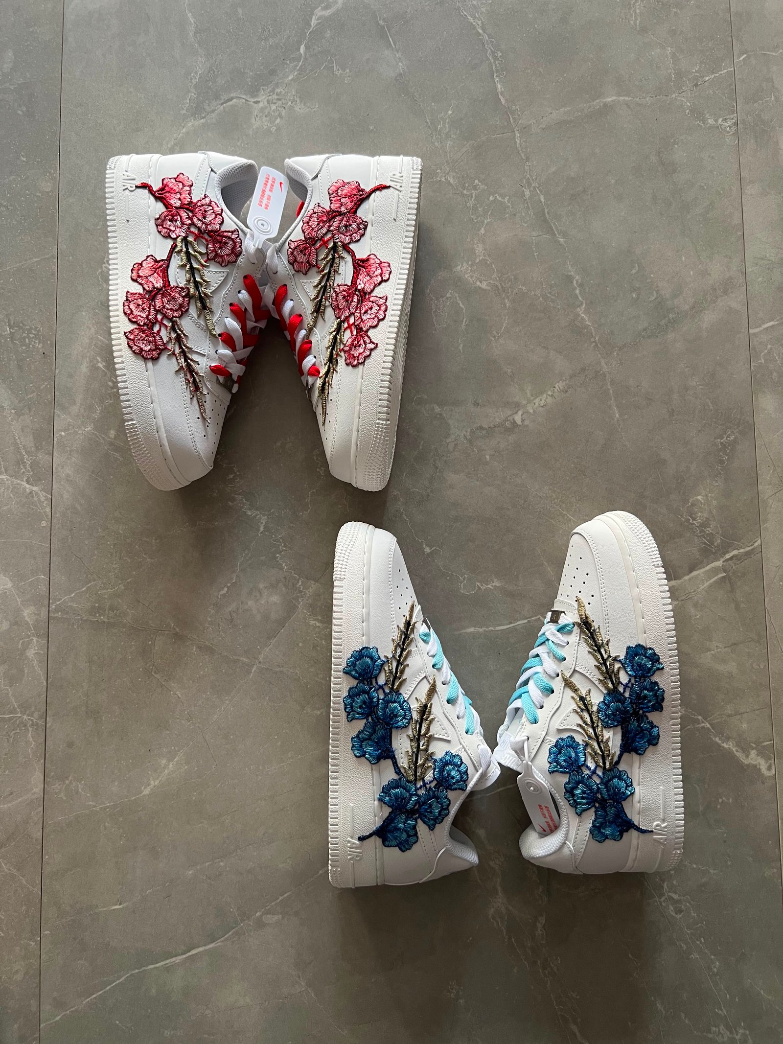 White low-top sneakers with raised floral embroidery in red-pink and deep blue colourways