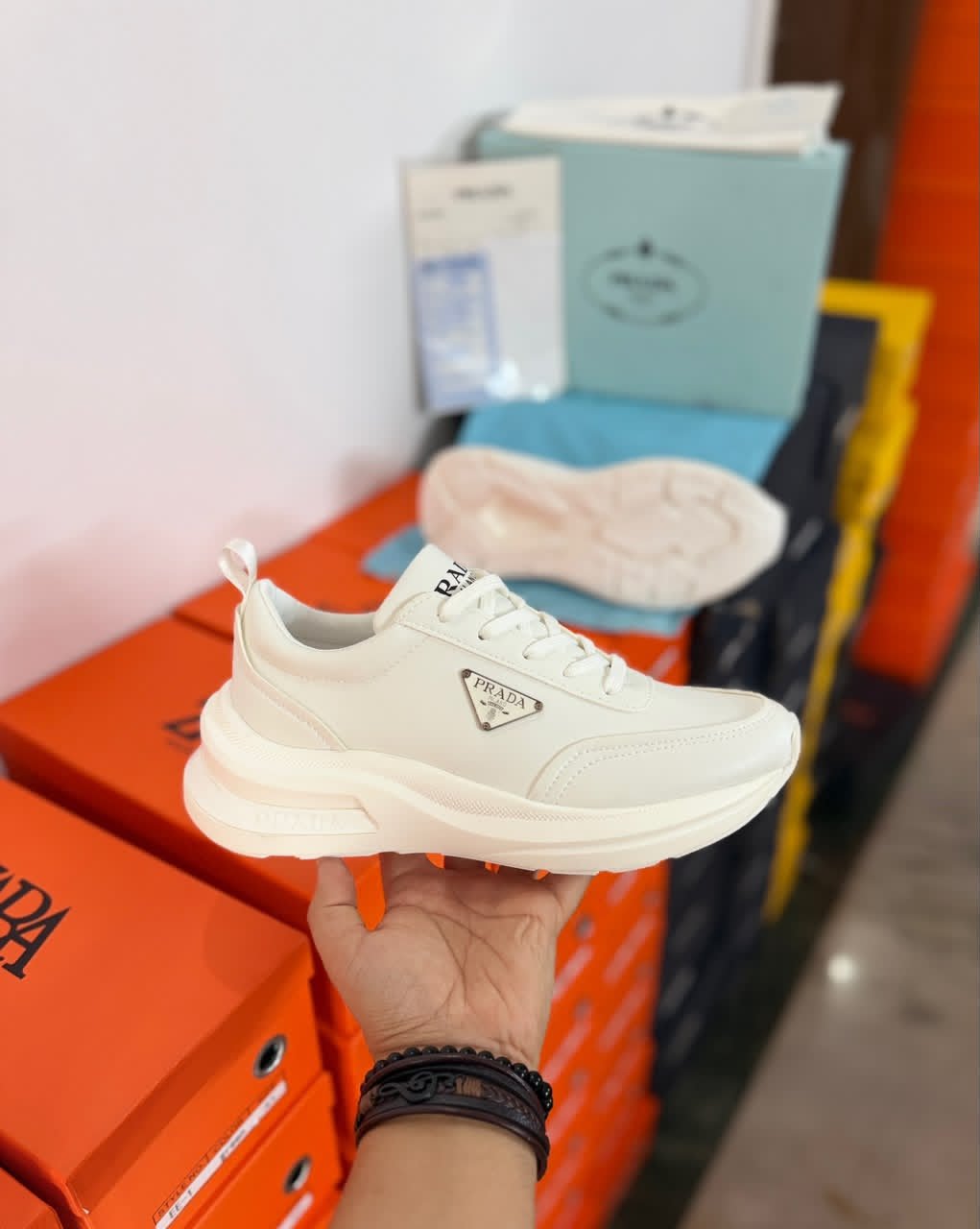 White minimalist low-top sneakers with a sculpted chunky sole, tonal panels, lace-up closure, and decorative side emblem