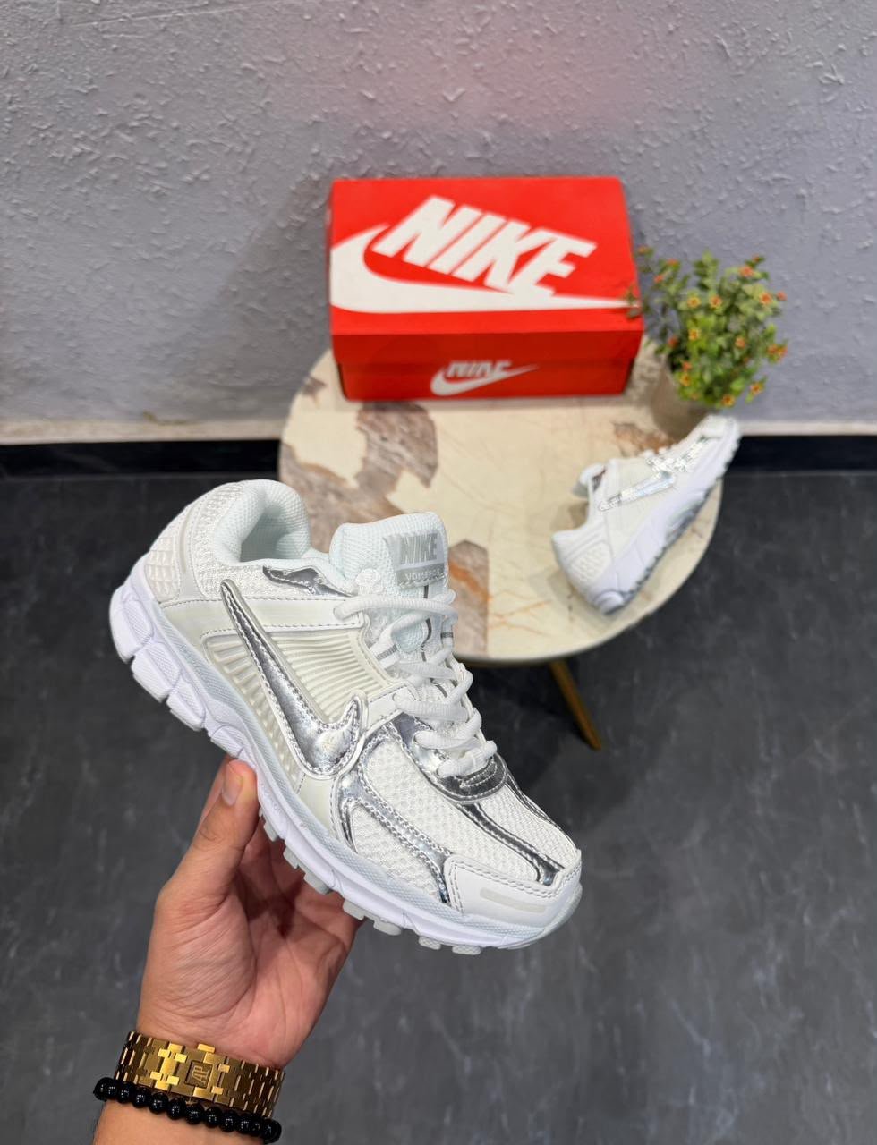 White sneakers with metallic silver swoosh detailing, layered panels, and chunky white soles